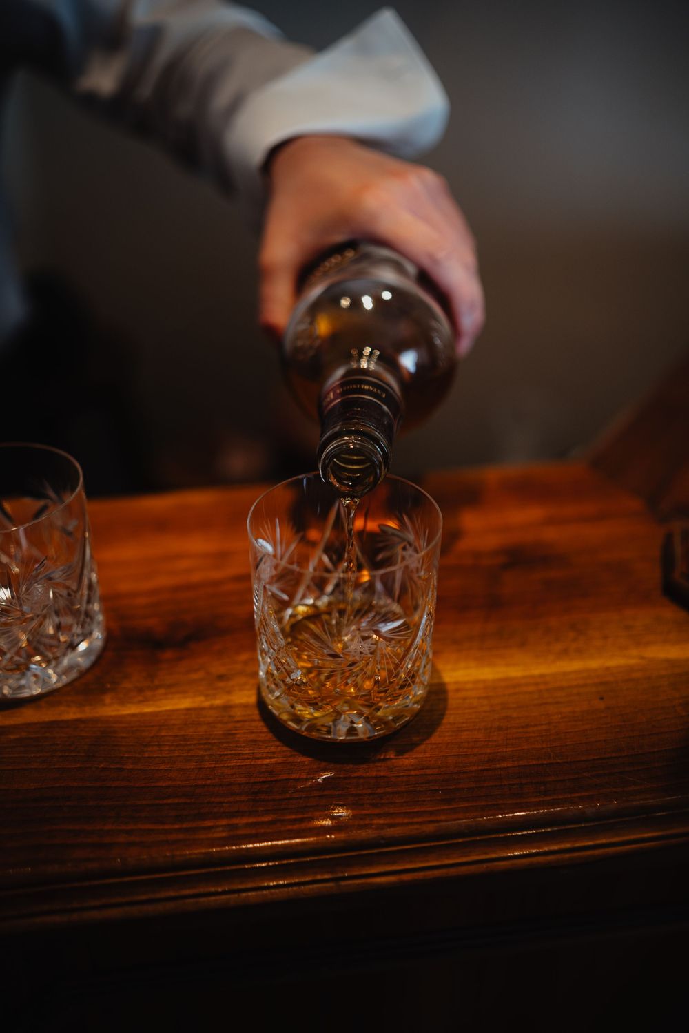 Whiskey being poured into a crystal glass on a dark wooden surface with atmospheric lighting.