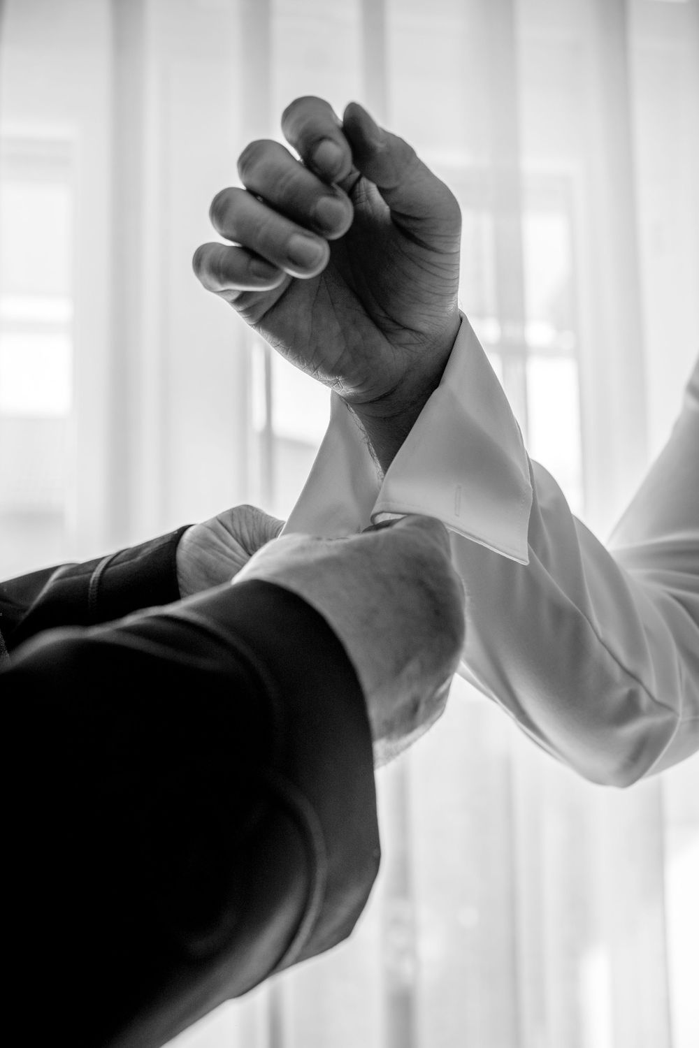 Two hands with dark and light sleeves grip each other in a celebratory arm wrestling or victory pose in black and white.