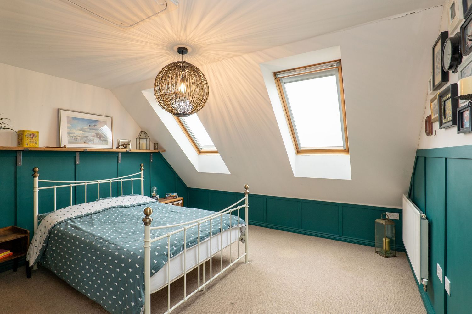 Cozy attic bedroom with teal wainscoting, white metal bed frame, and pendant lighting under sloped ceiling.