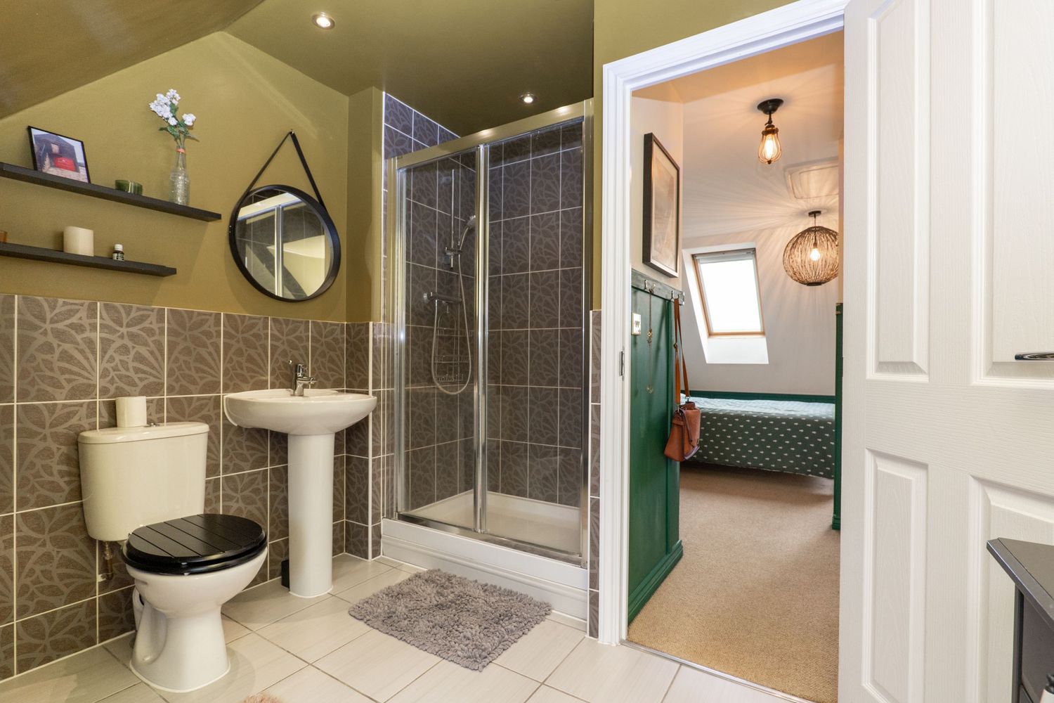 Modern bathroom with grey tile, pedestal sink, glass shower enclosure and round mirror.