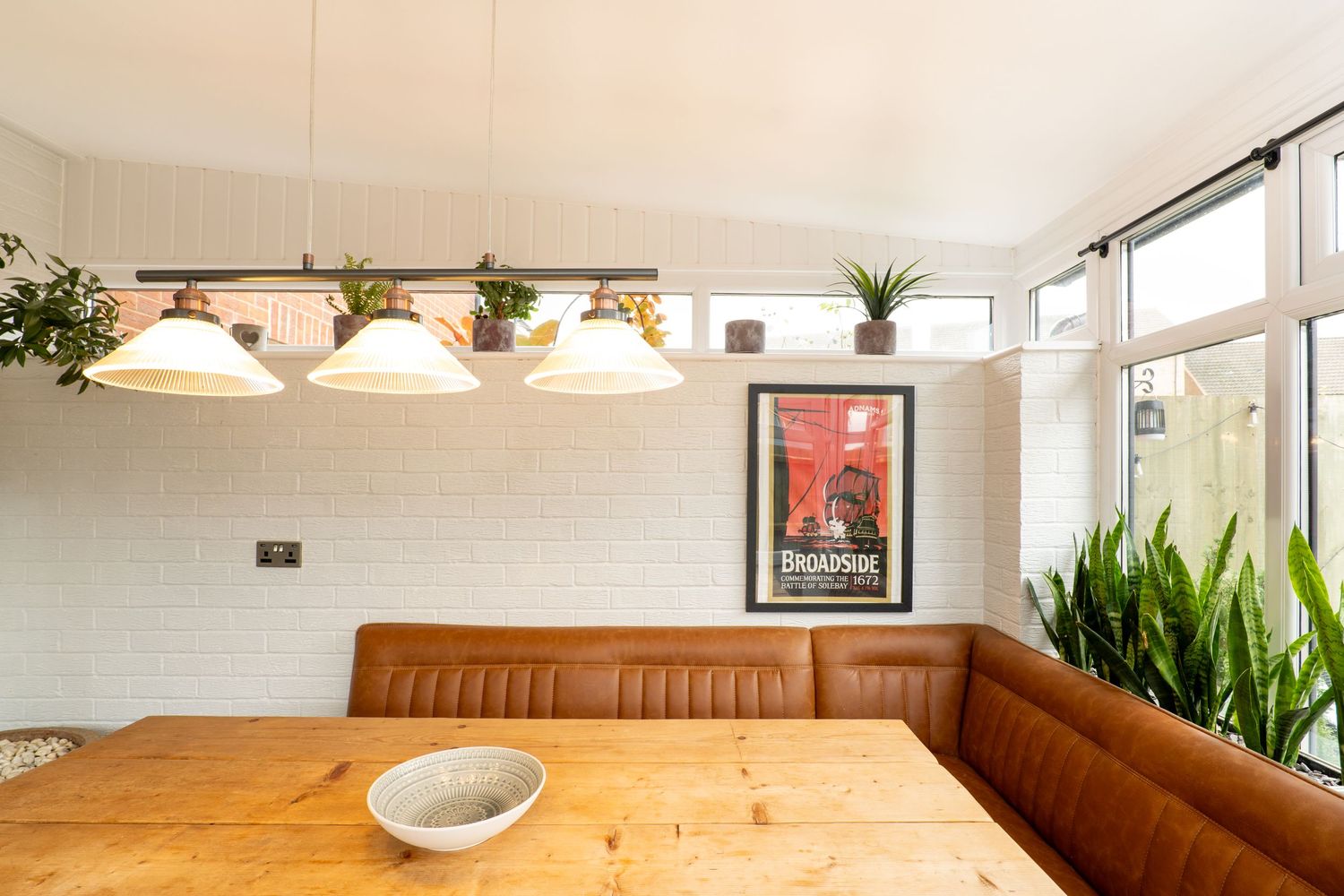Dining area with leather banquette seating, wooden table, and pendant lights along a window wall.