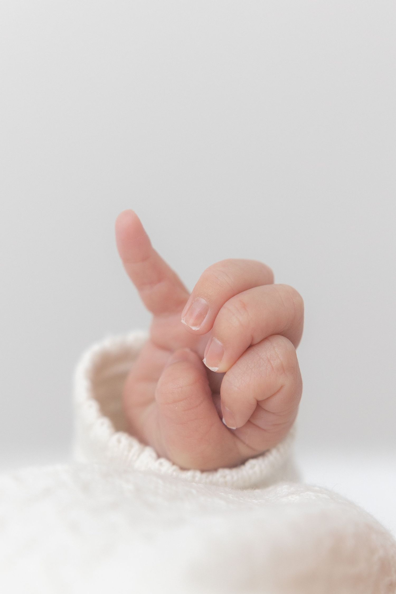 A tiny baby's hand emerges from white knit fabric, reaching up with delicate fingers against a soft light background.