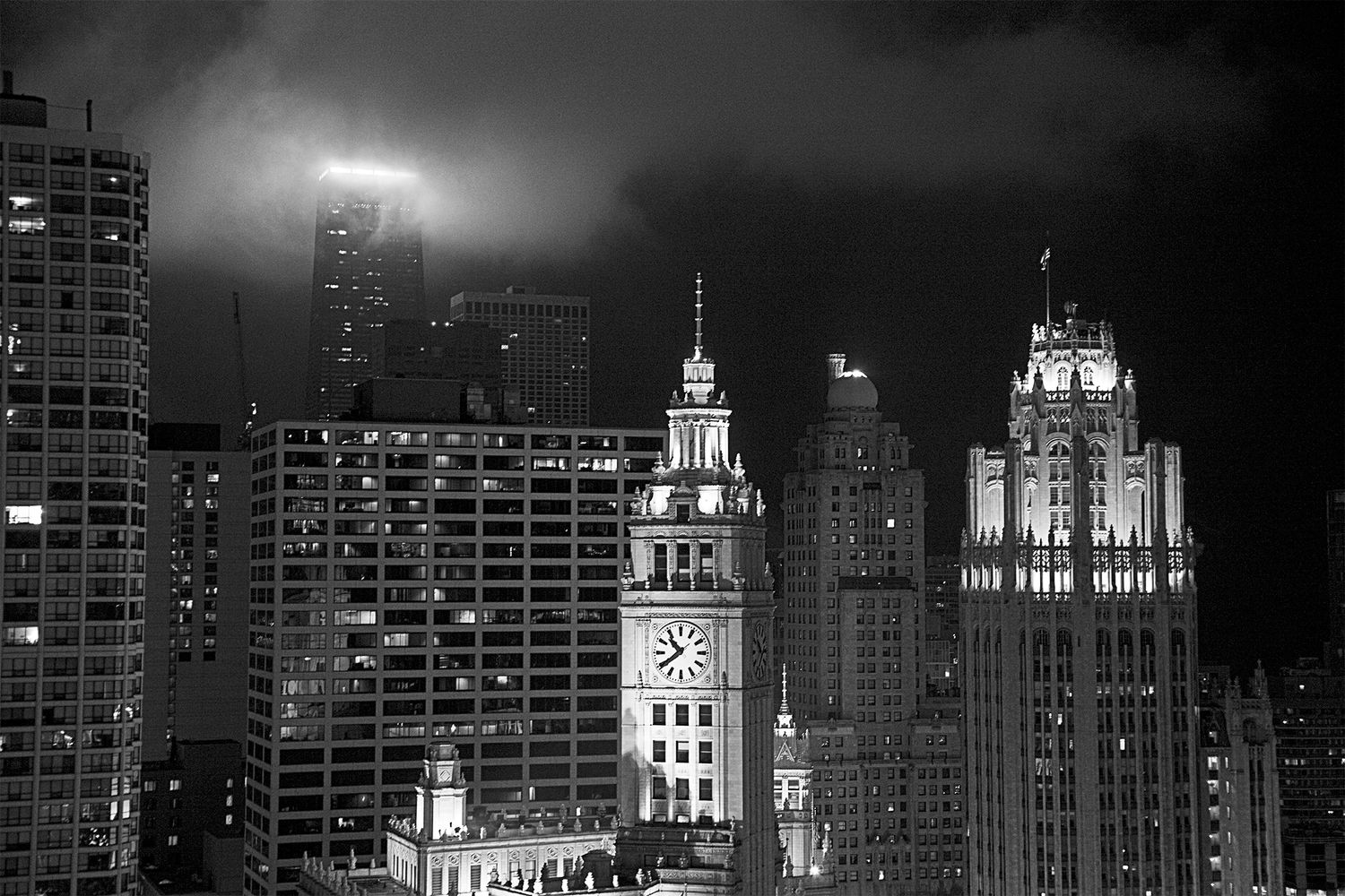 Moody black and white cityscape of Chicago with illuminated historic buildings in fog.