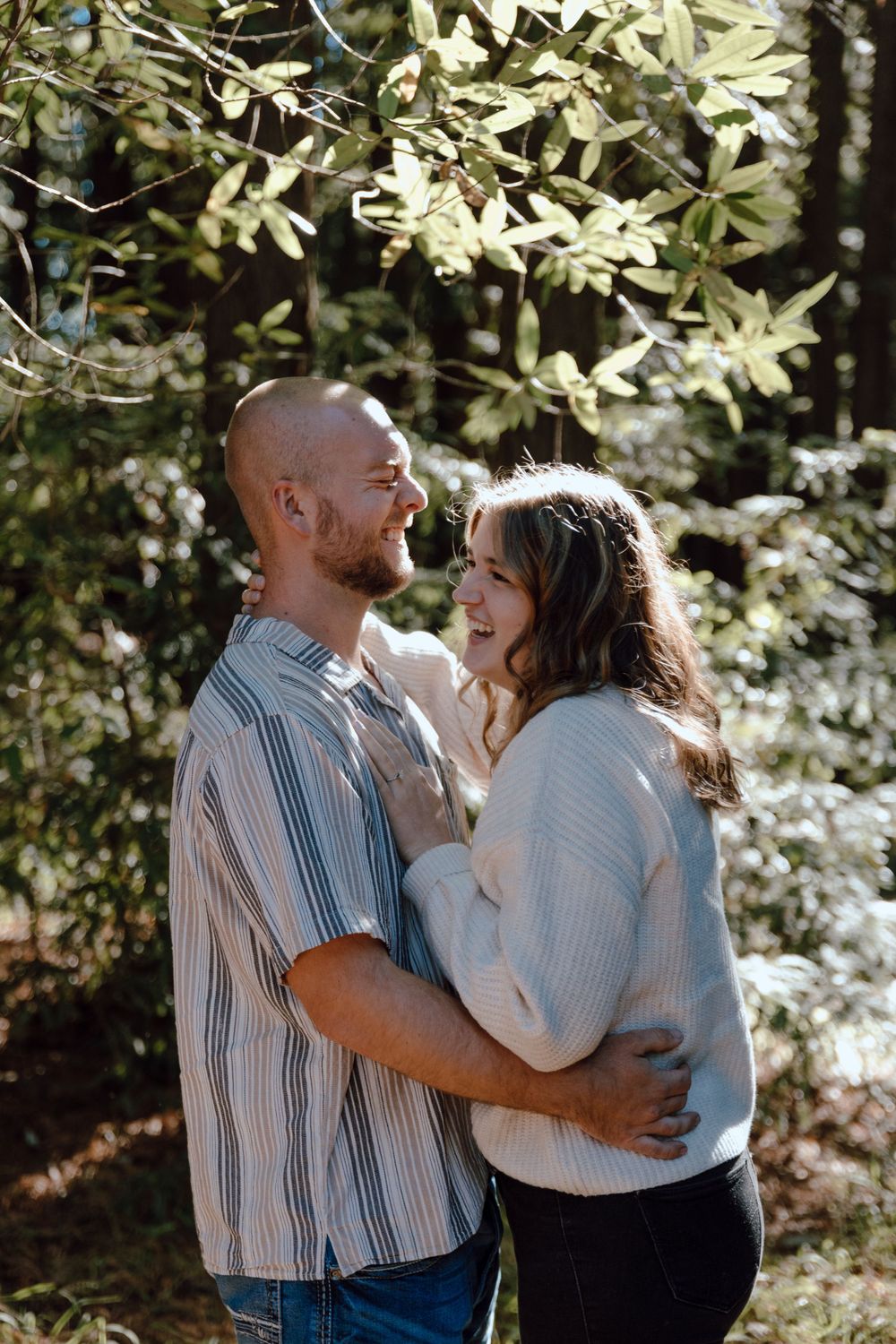 Romantic couple embraces and shares a tender moment outdoors under flowering trees on a sunny afternoon.