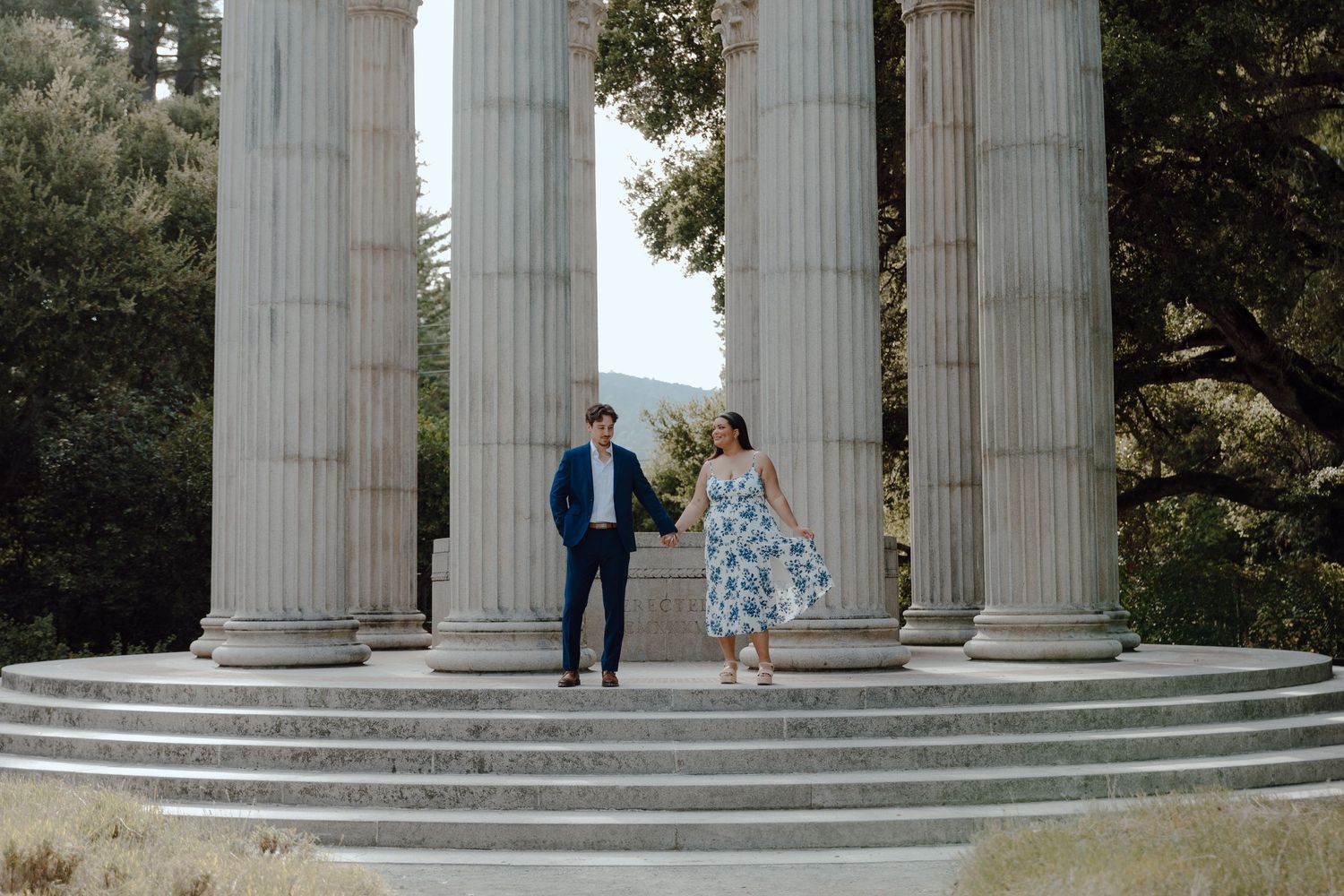 Two people stand between classical white stone columns and steps at an elegant outdoor monument location.