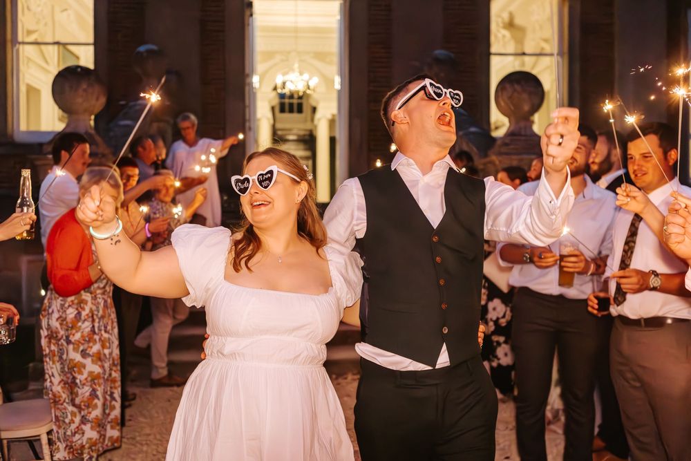 Happy couple shares romantic dance at wedding reception while guests hold sparklers creating magical nighttime atmosphere.