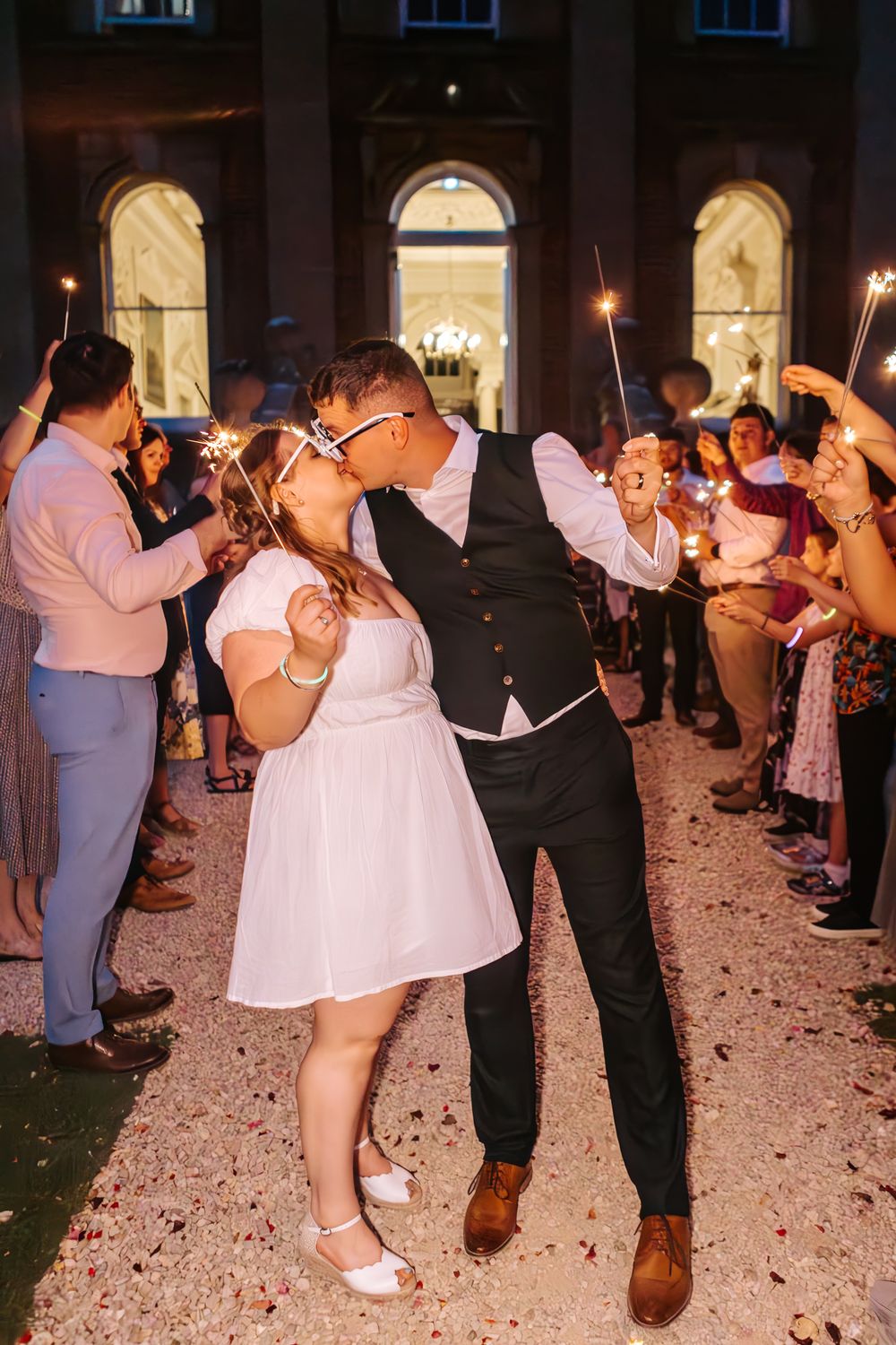 Multiple couples dance together in an indoor venue with rose petals scattered on the floor.