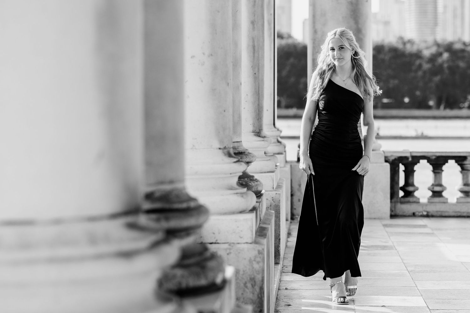 Elegant black and white photo of a woman in a long black dress standing between classical stone columns.