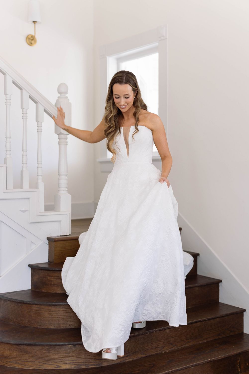 An elegant white wedding gown with strapless design and full skirt seen on wooden staircase in bright interior.