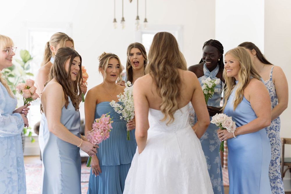 A bride in a white gown surrounded by bridesmaids wearing light blue dresses at a wedding celebration.