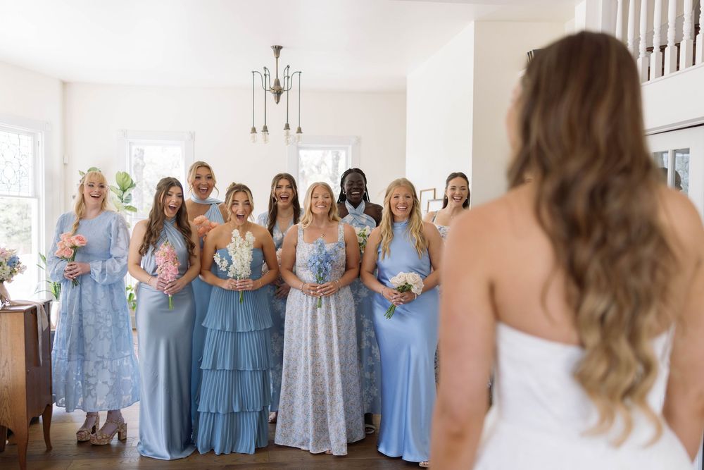 Bridesmaids in flowing blue and floral dresses stand together holding bouquets during a wedding ceremony.