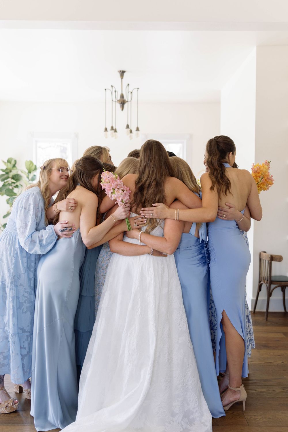 A group in light blue bridesmaid dresses huddle together with someone in a white wedding gown in an indoor setting.