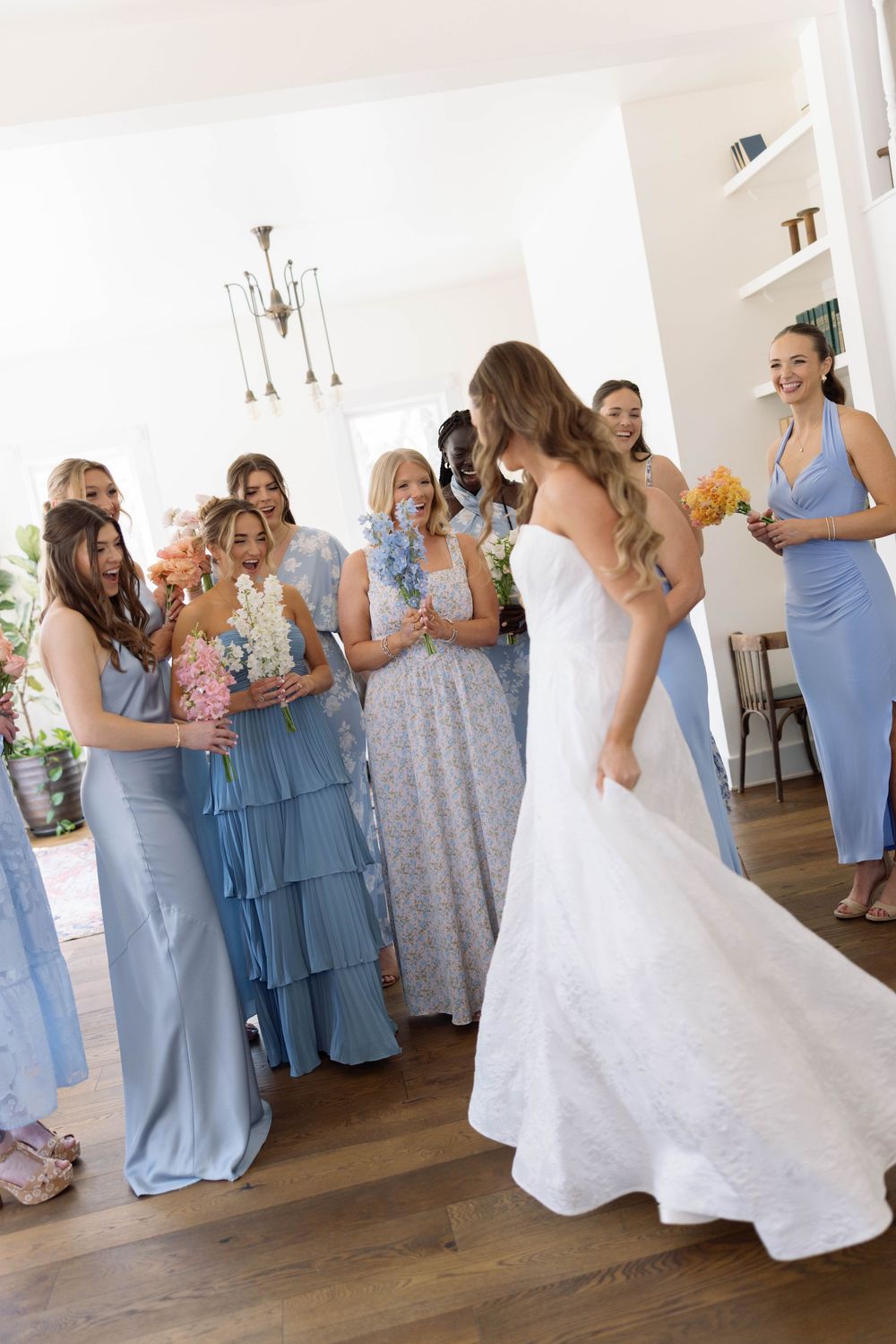 Bridesmaids in soft blue dresses gather around a bride in a white gown during a wedding celebration.