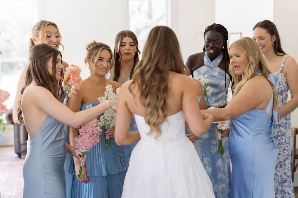 A group of bridesmaids in light blue dresses gather around a bride in a white wedding gown during a celebration.