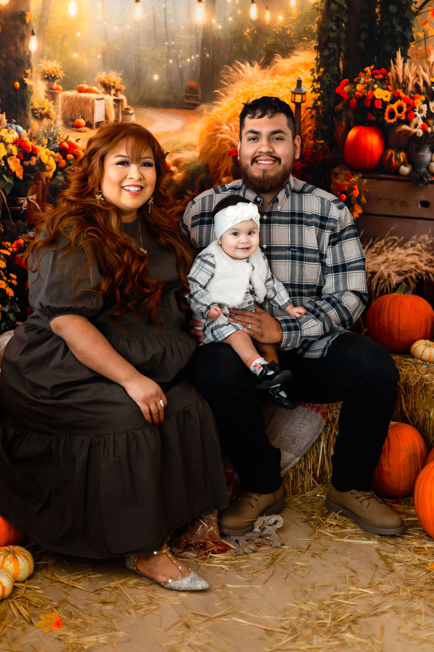 A cozy fall family portrait featuring pumpkins, hay bales, and warm lighting in a rustic autumn-themed setting.