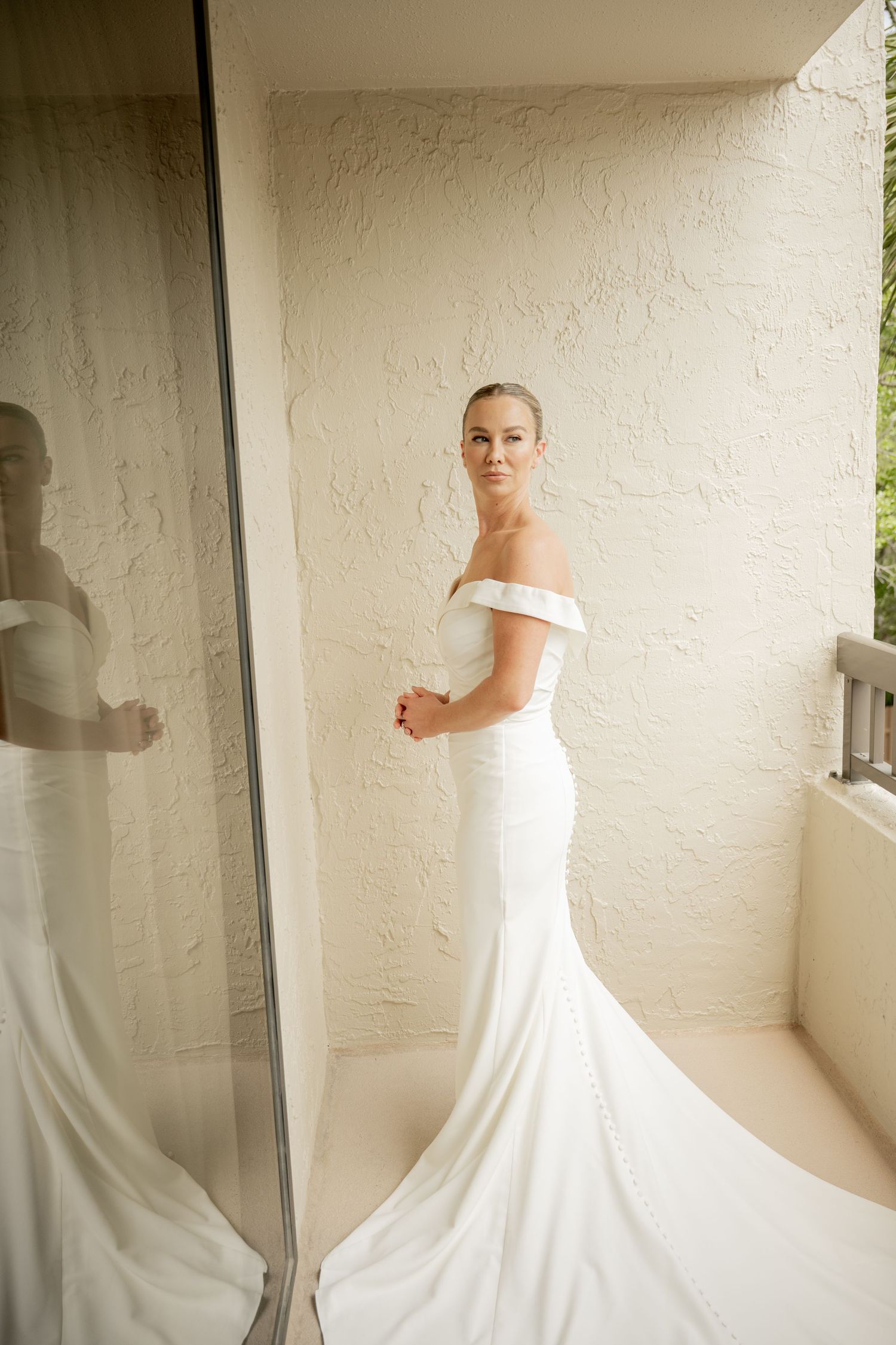Couple in wedding attire standing apart on a path surrounded by palm trees and Spanish moss in a garden setting.