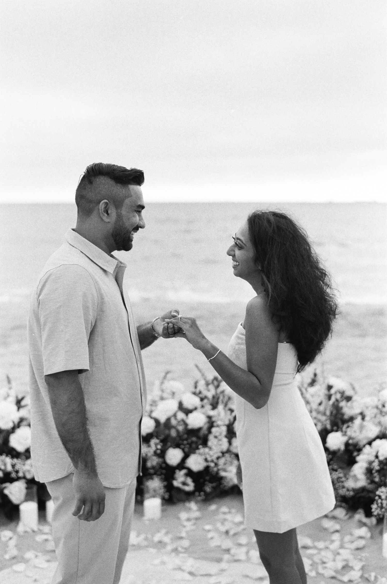 A couple shares a joyful moment on the beach surrounded by floral decorations.