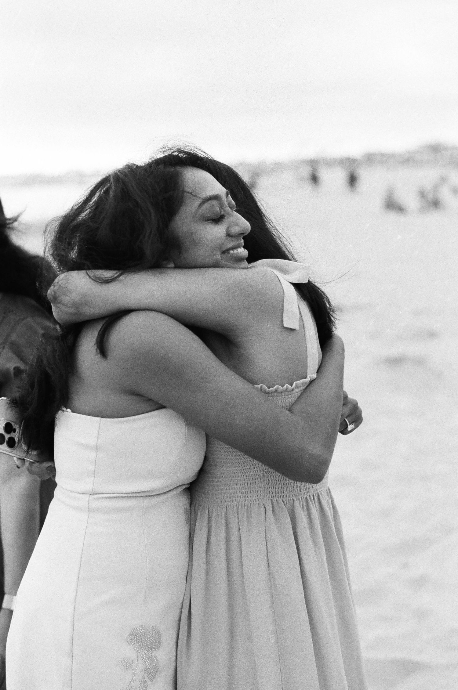 Two people embracing warmly on a sunny beach in white dresses.