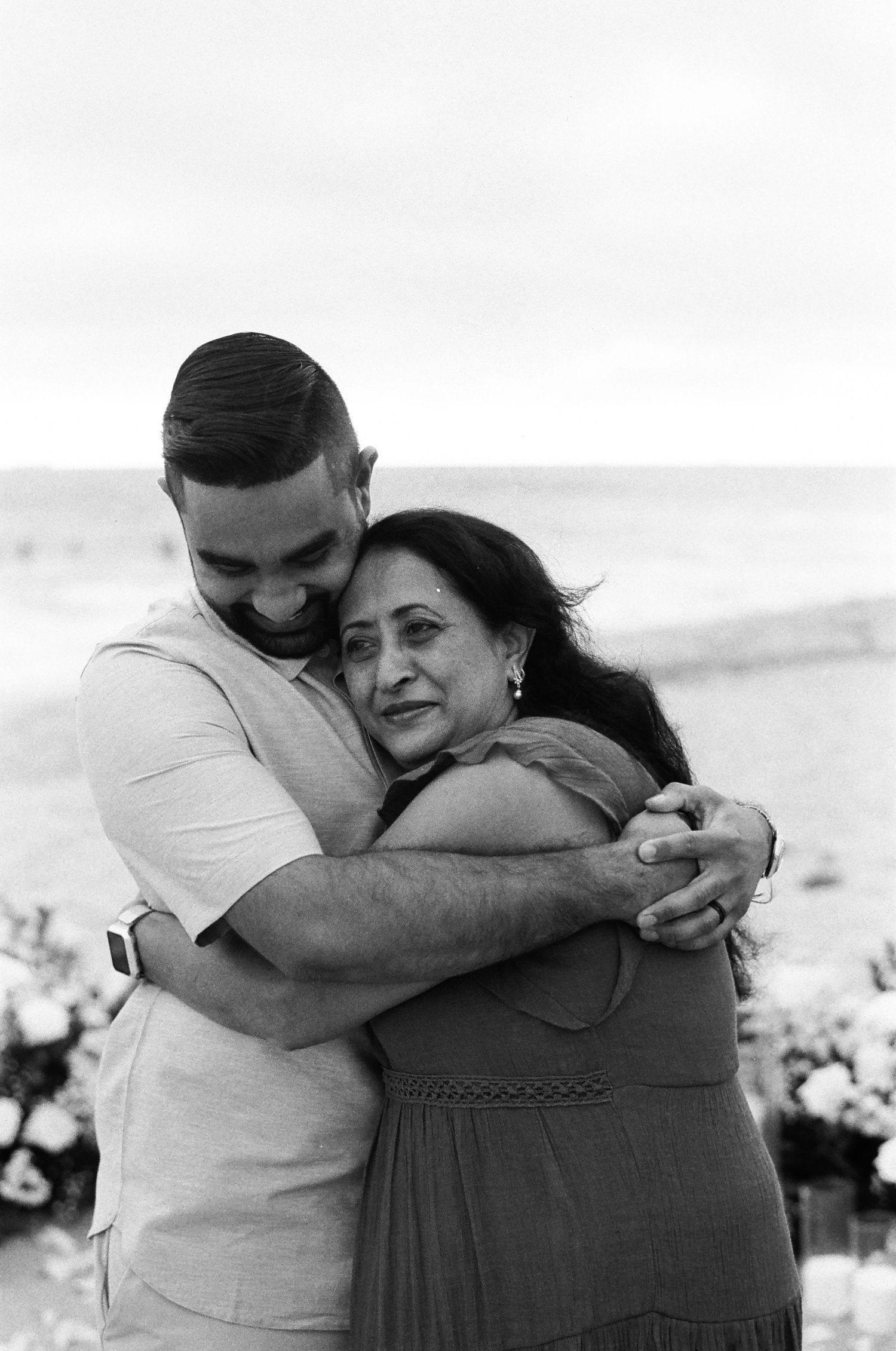A tender black and white portrait shows an intimate embrace between two people outdoors in a loving moment.