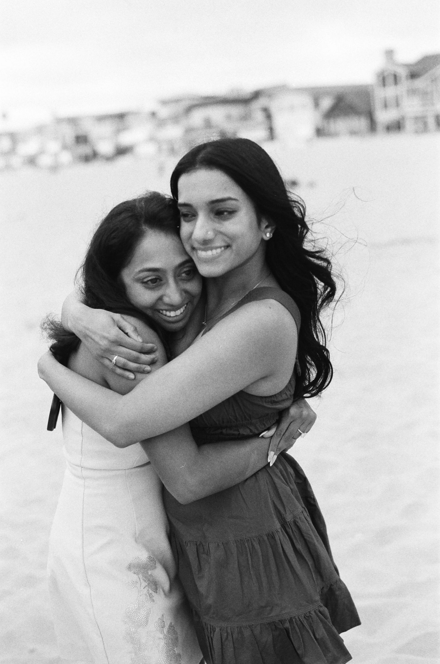 Two friends sharing a joyful embrace on the beach in a heartwarming black and white photograph.