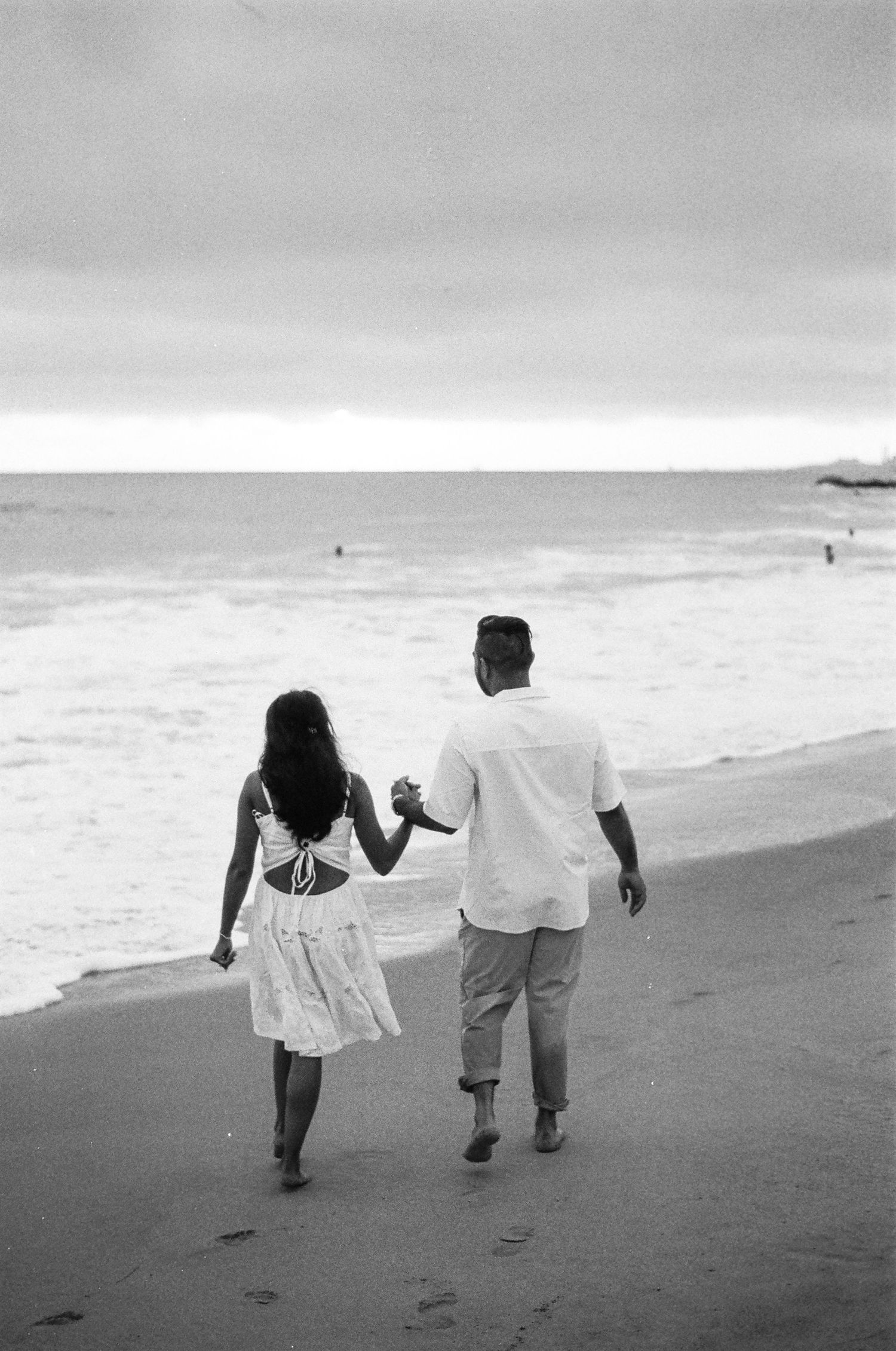 A couple holding hands while walking along the shoreline in black and white.