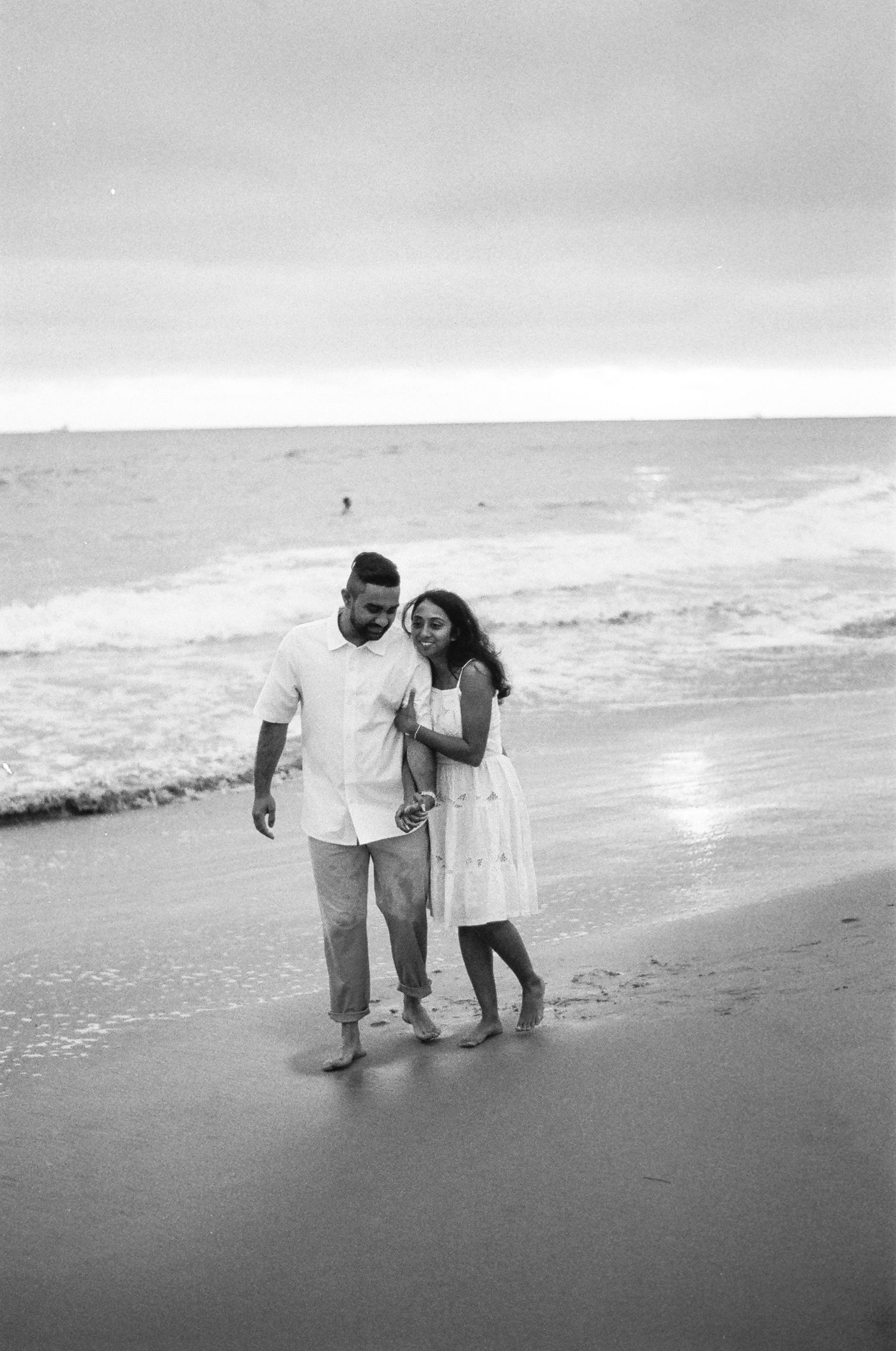 Black and white photo of people walking along a beach shore at sunset.