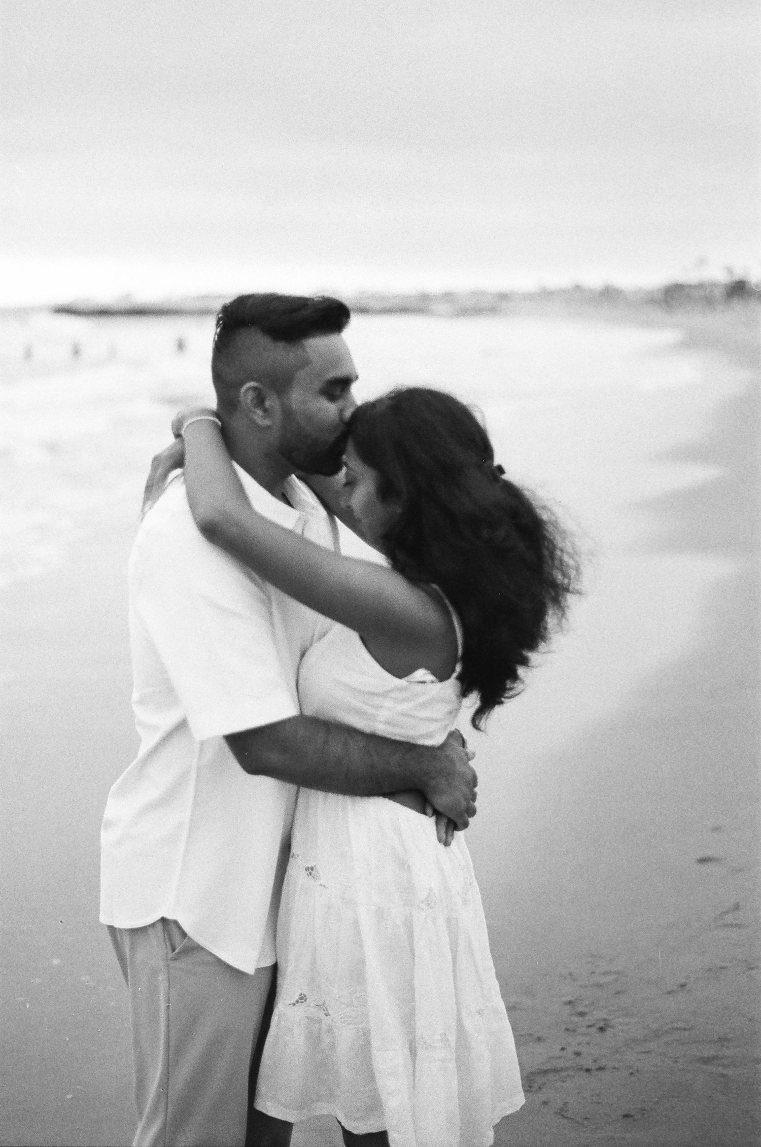 An intimate moment shared between a couple embracing on a misty beach.