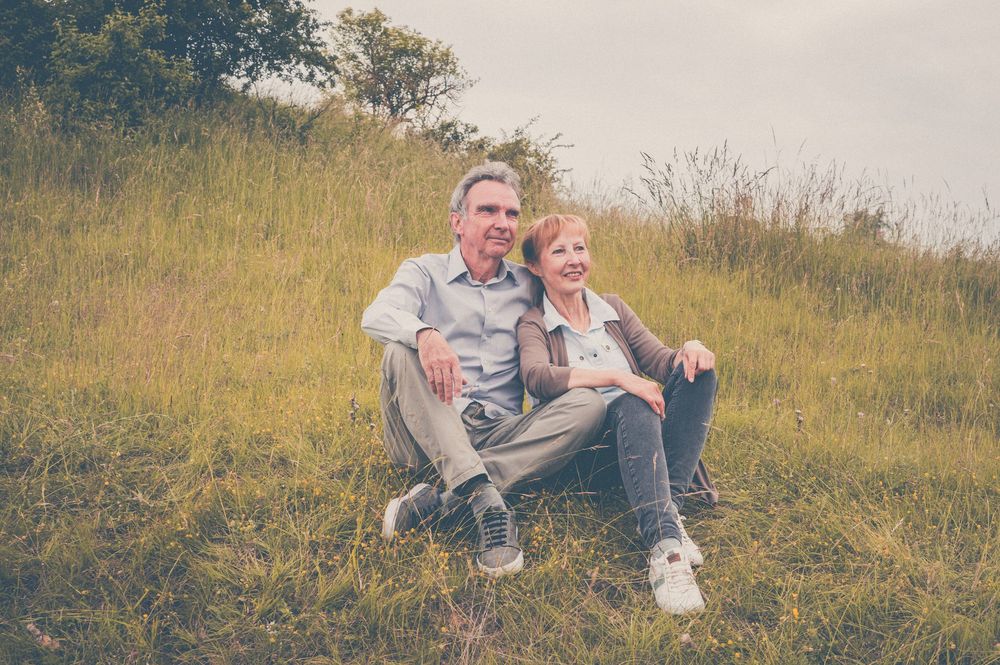 Two people sitting casually together on a grassy hillside on an overcast day.