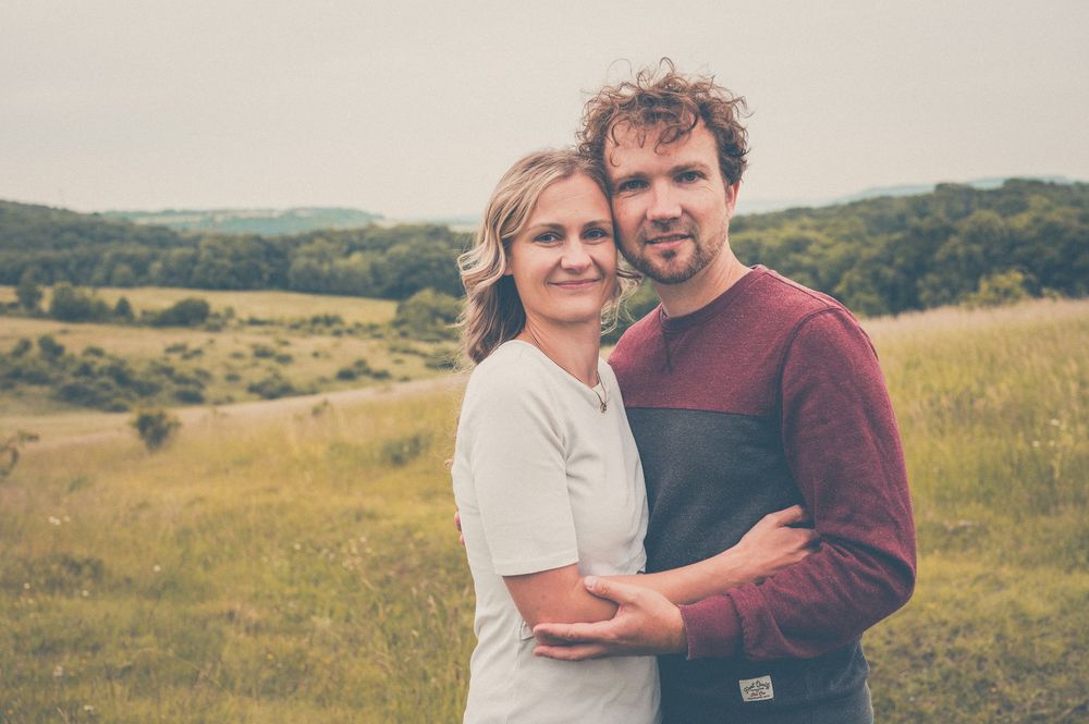 Two people embracing in a romantic pose against a backdrop of rolling hills and autumn trees.