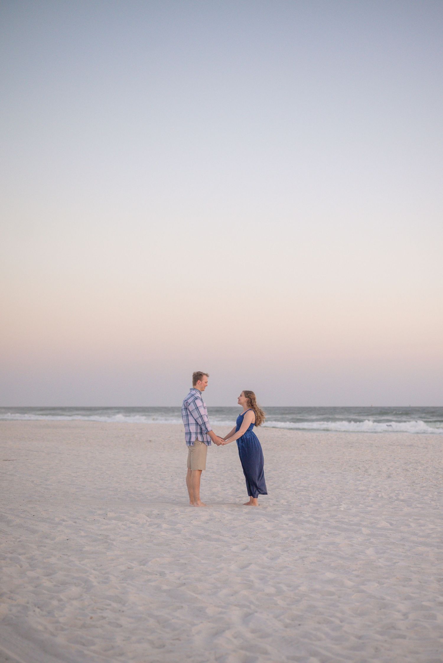 Two silhouettes stand together on empty beach at dusk.