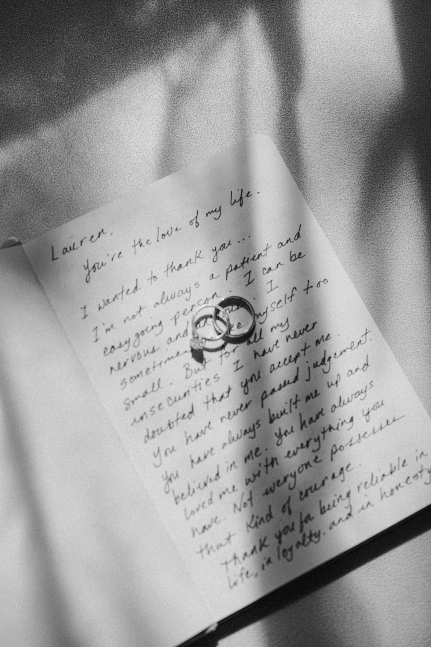 Black and white photo of wedding rings resting on a handwritten love letter.