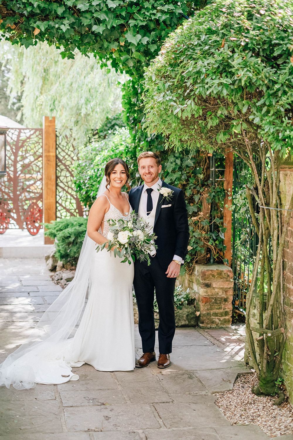 A couple poses for wedding photos on a garden path framed by lush greenery.