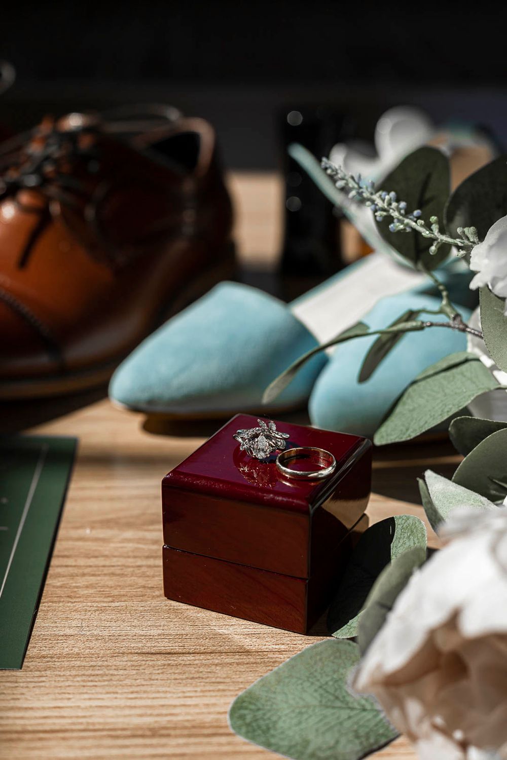 Wedding ring in burgundy box with blue shoes and eucalyptus details.