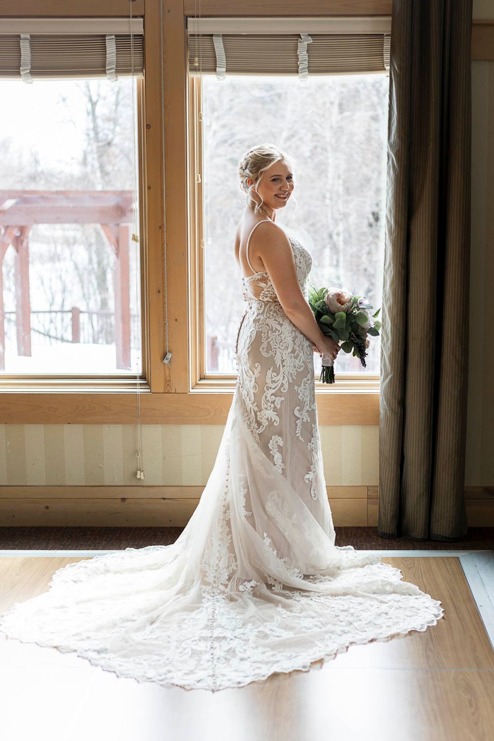 Beautiful lace wedding gown with long train photographed against snowy window backdrop.
