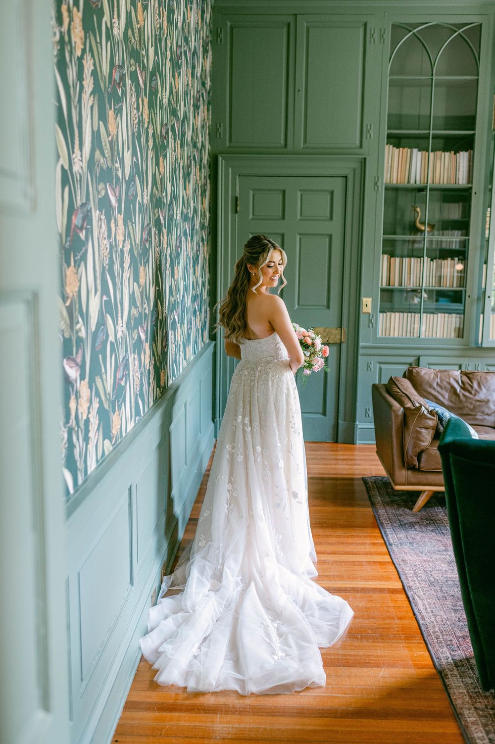 A bride in a flowing white lace wedding dress twirls in a room with mint green walls and hardwood floors.