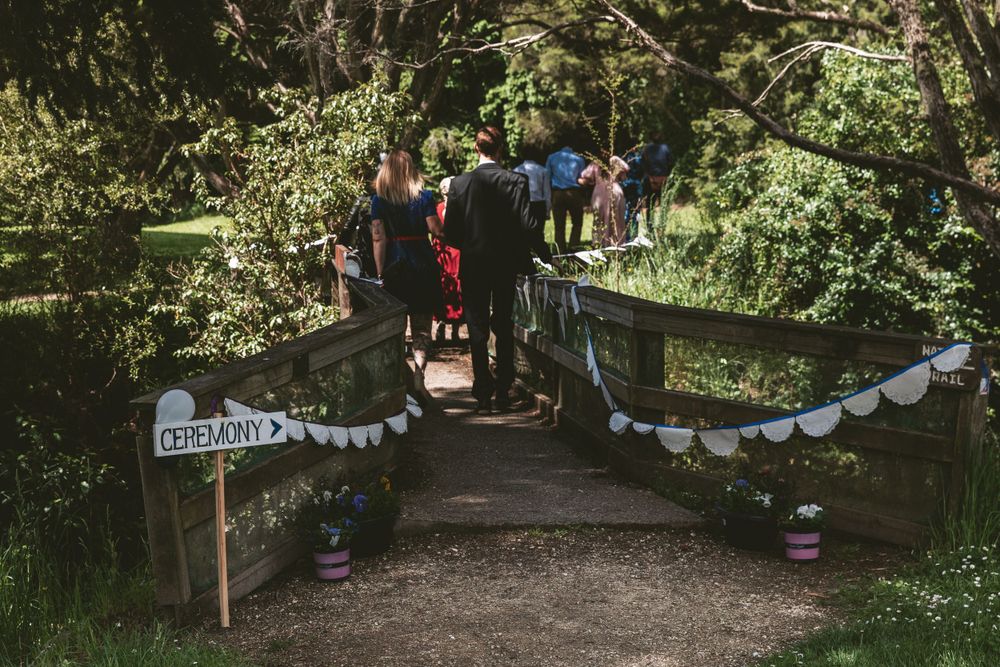 Wedding decorations with white bunting along wooden bridge path in forest setting.