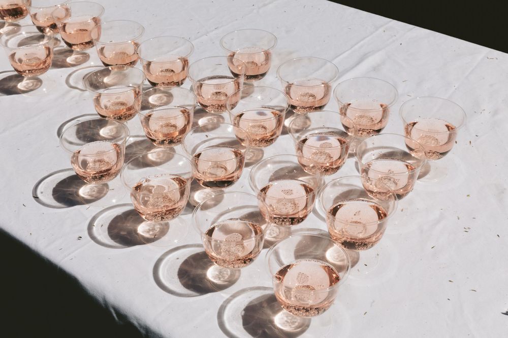 Rows of pink champagne glasses arranged on white tablecloth casting afternoon shadows.
