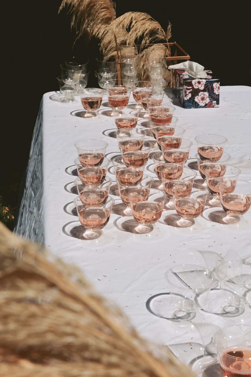 Elegant display of rose-colored champagne glasses with pampas grass decoration on white tablecloth.