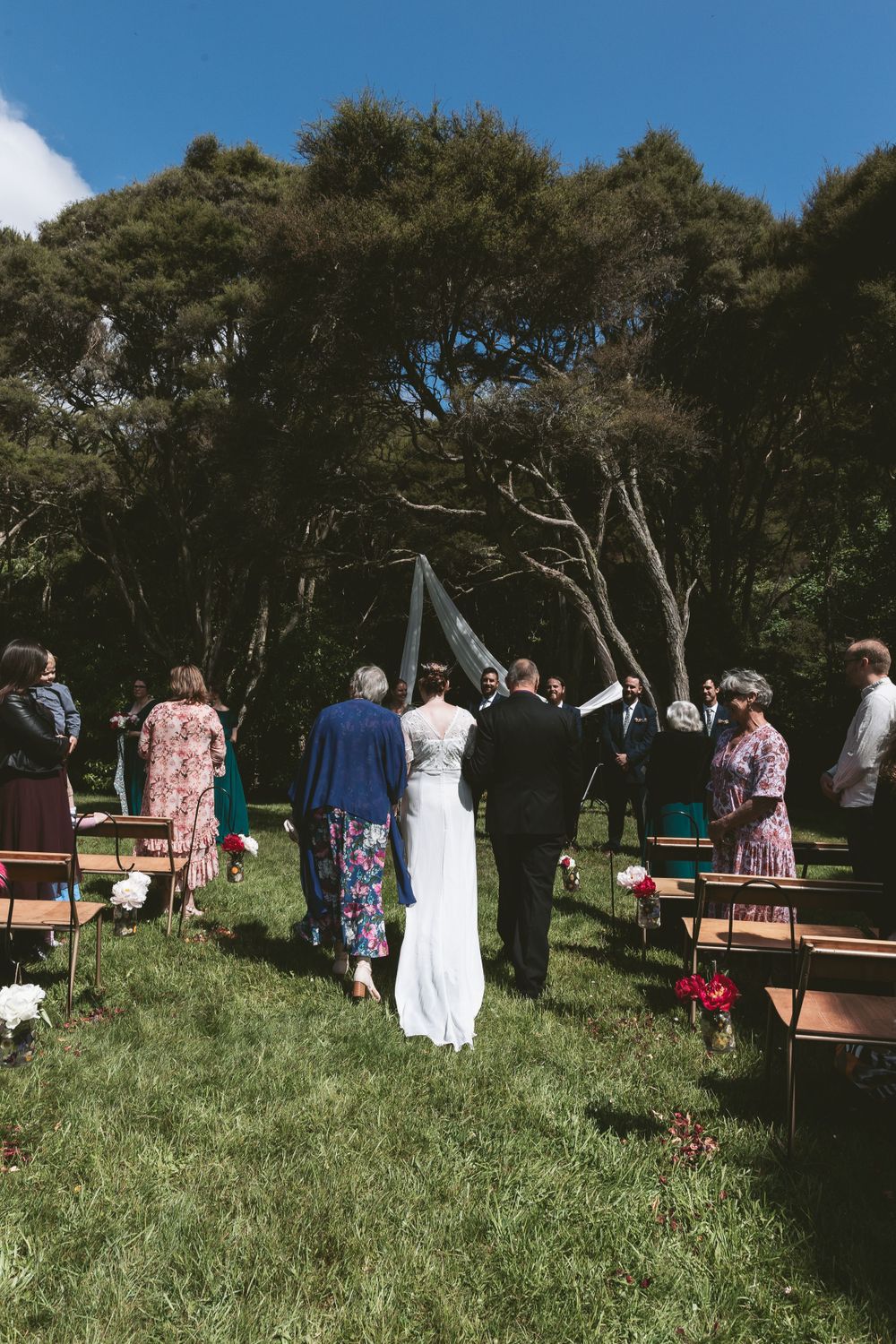 Outdoor wedding ceremony setup with folding chairs and draped fabric arch among tall trees.