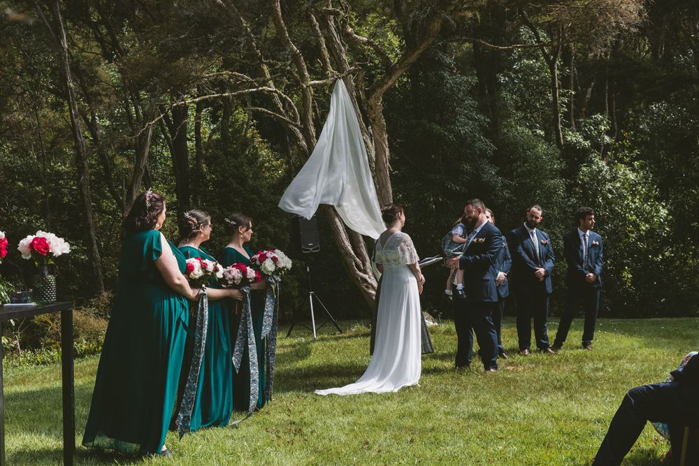 Wedding party arranged at outdoor ceremony with bridesmaids in emerald green dresses standing in a row.