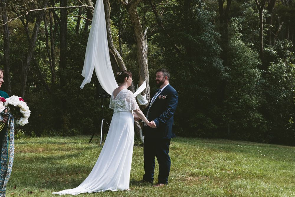 Outdoor wedding ceremony with white fabric draping from trees and floral arrangements.