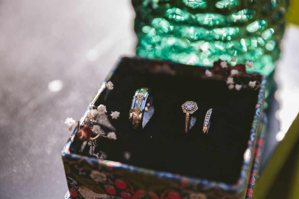 Wedding rings displayed on dark velvet cushion with emerald green fabric in background.