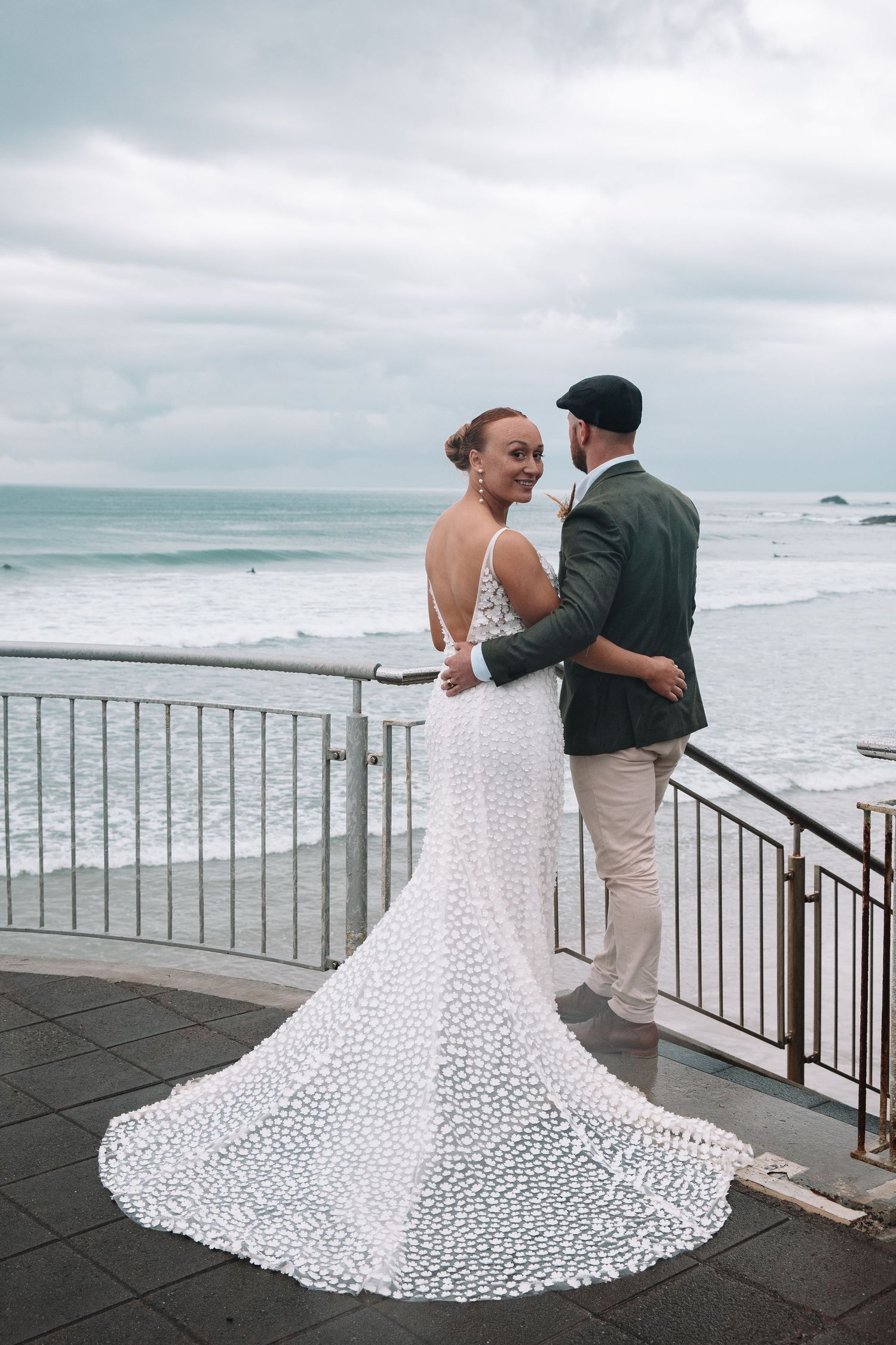 Couple embraces on oceanfront terrace with dramatic white lace wedding dress train.