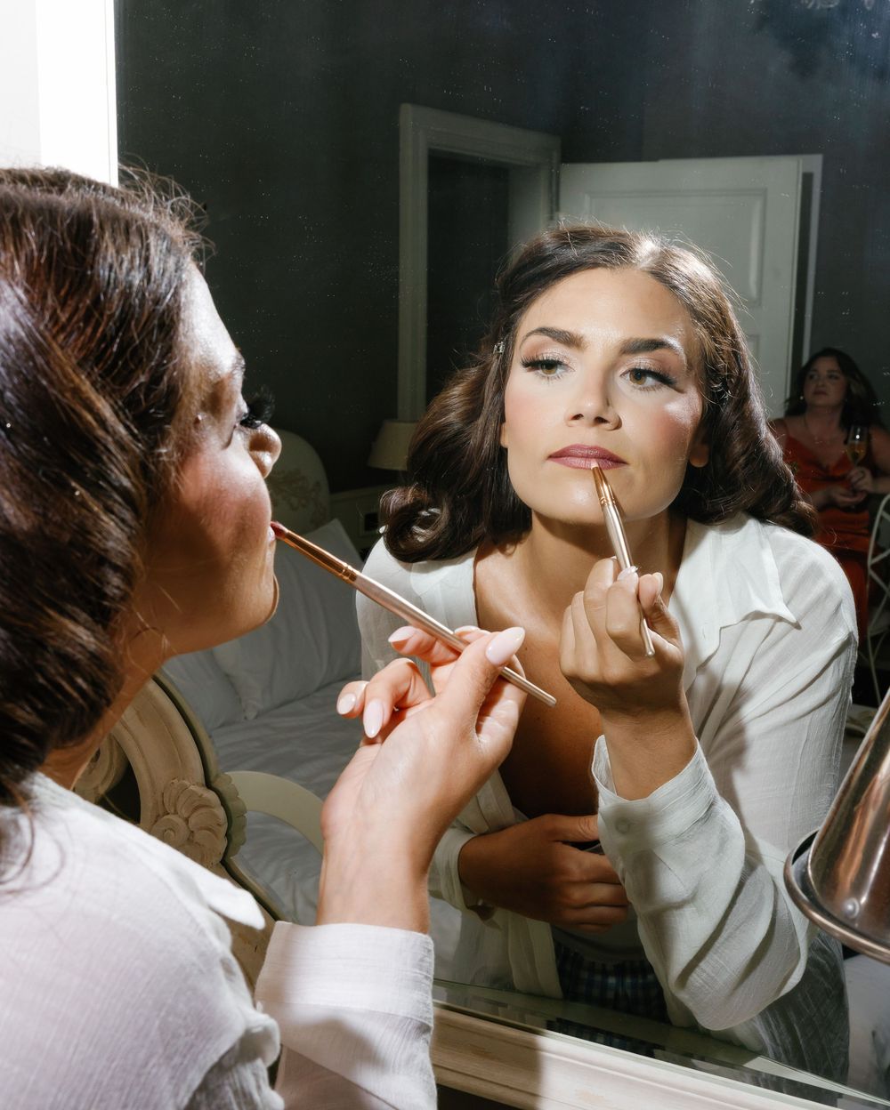 Beauty model having makeup professionally applied with brush while looking in mirror during cosmetic preparation session.