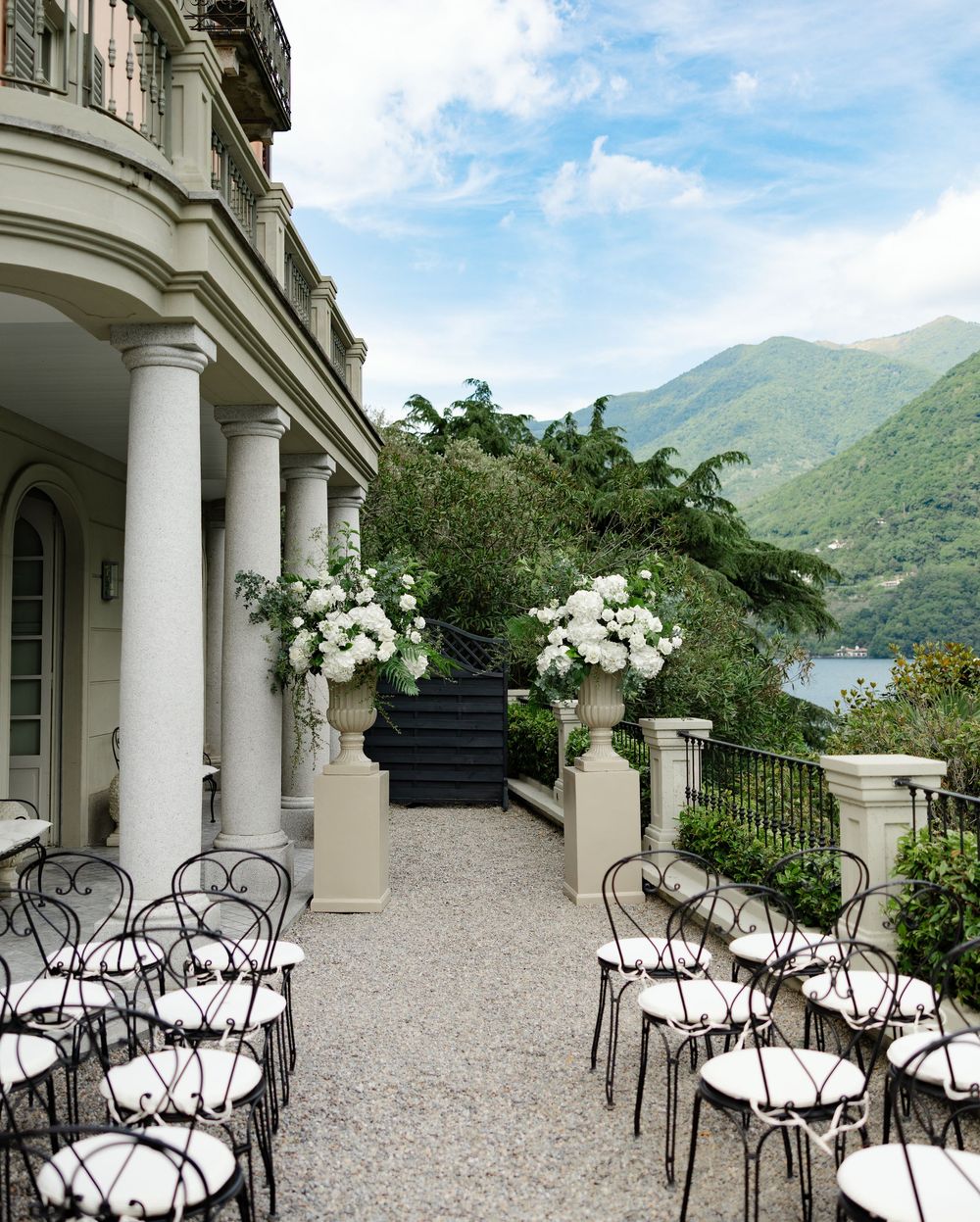 A set of elegant outdoor chairs with white cushions arranged on a terrace overlooking a scenic mountain lake view.