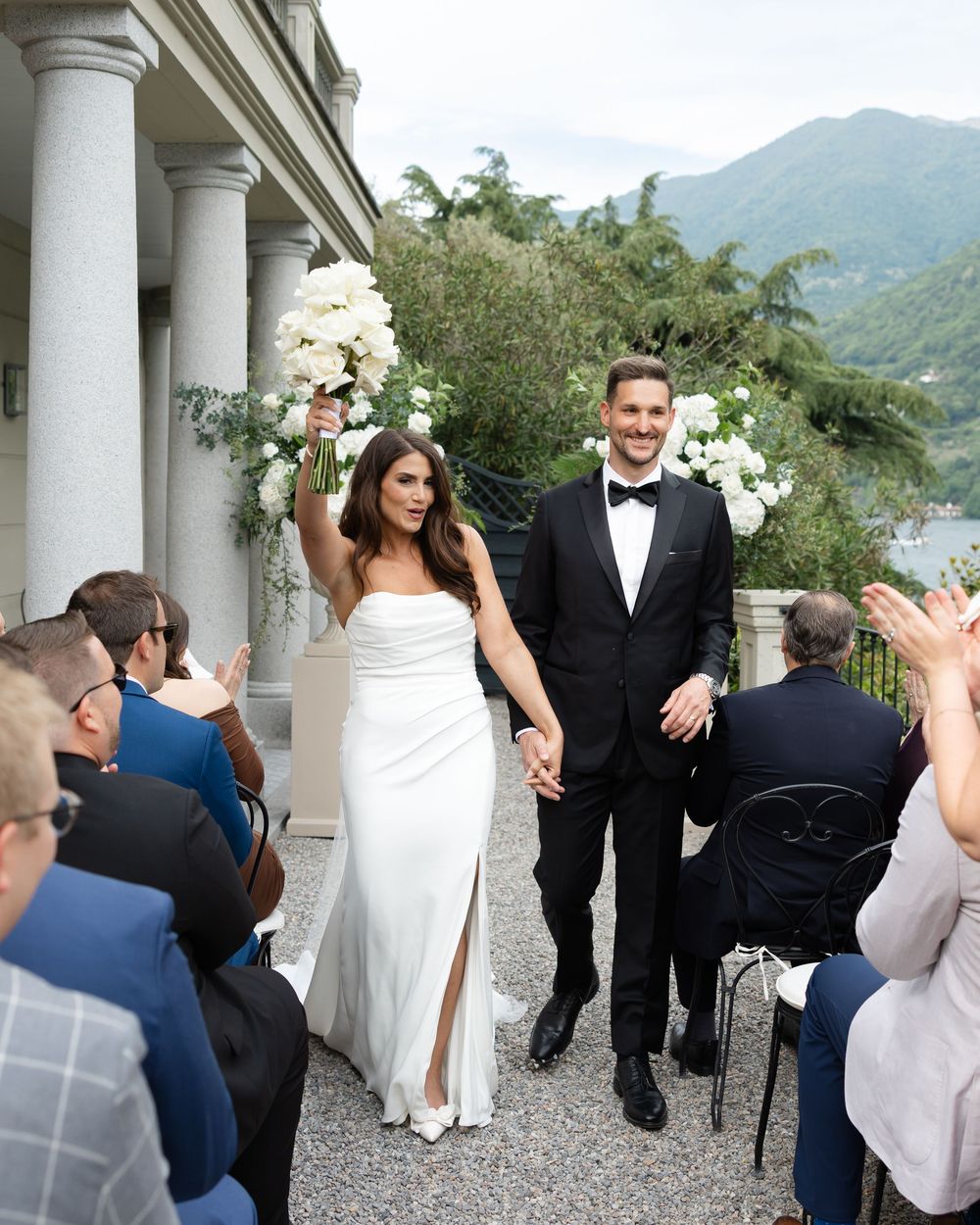 A wedding ceremony at a lakeside villa with white floral arrangements and classic columns in a mountain setting.