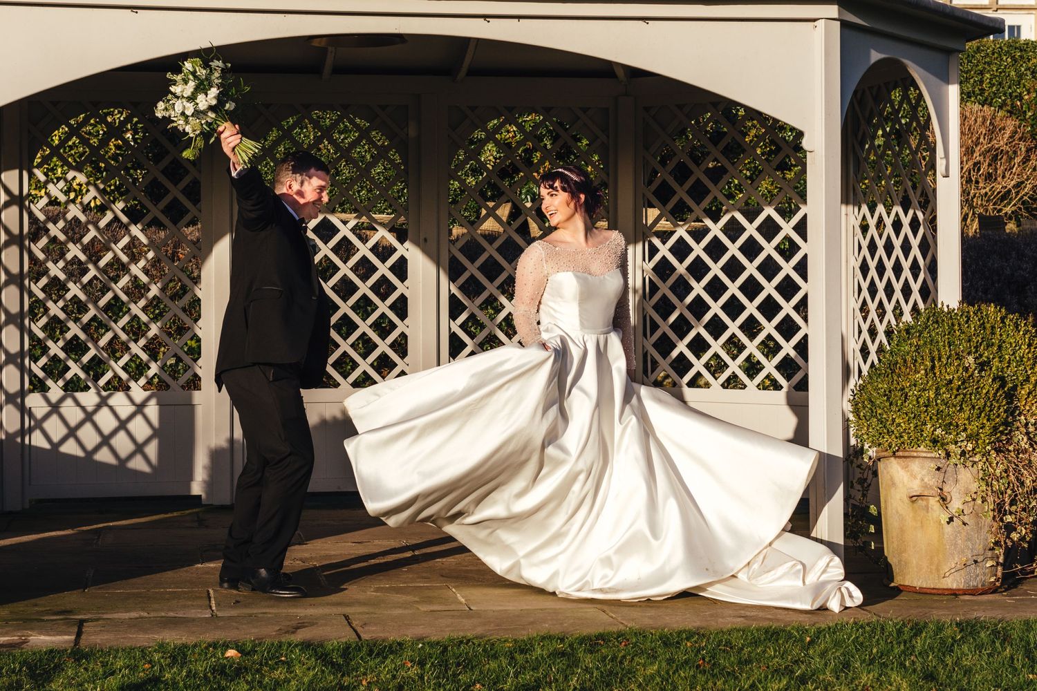 Couple playfully poses under garden pergola with flowing wedding dress.