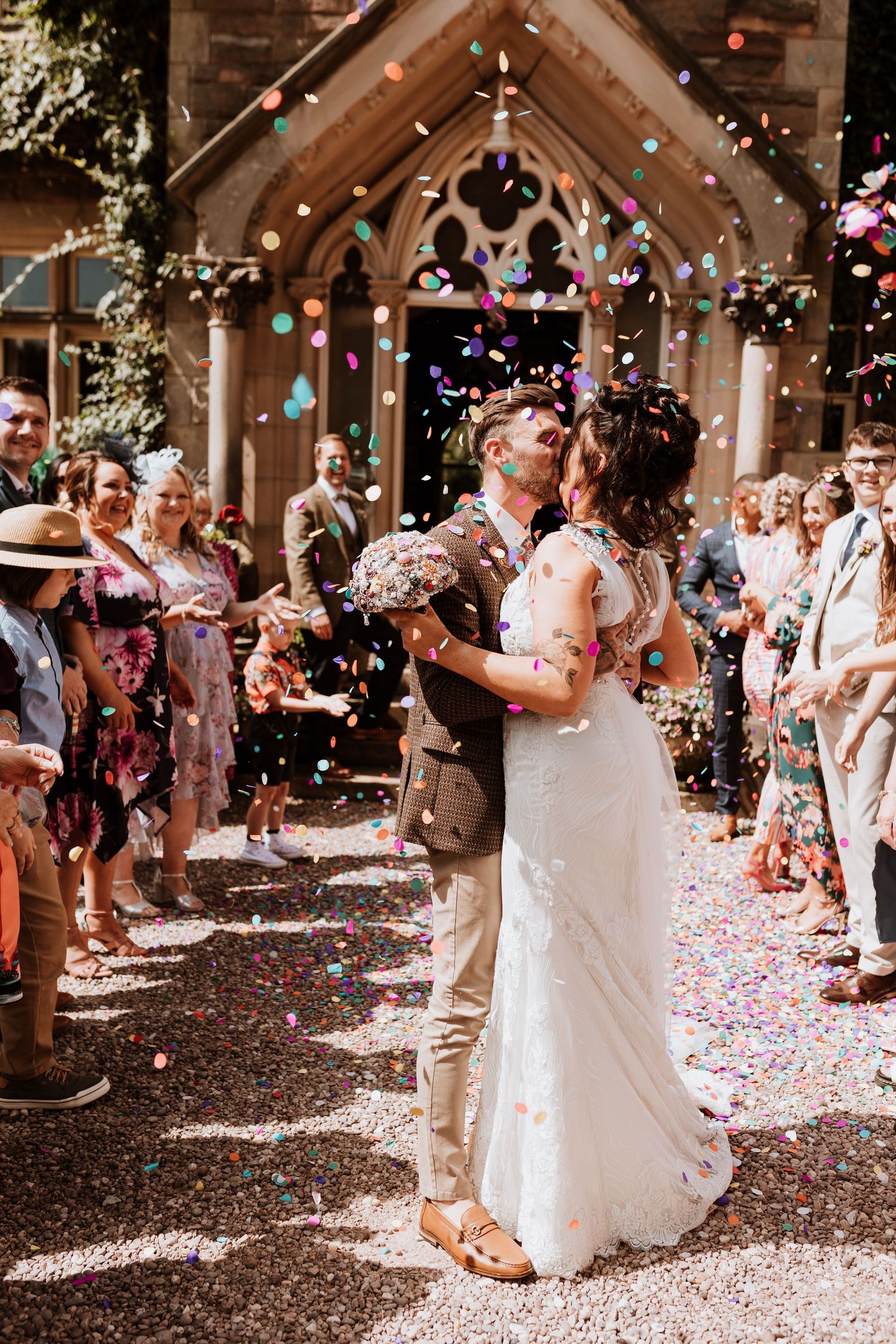 Wedding guests shower couple with pink and white confetti as they celebrate during outdoor ceremony exit celebration.