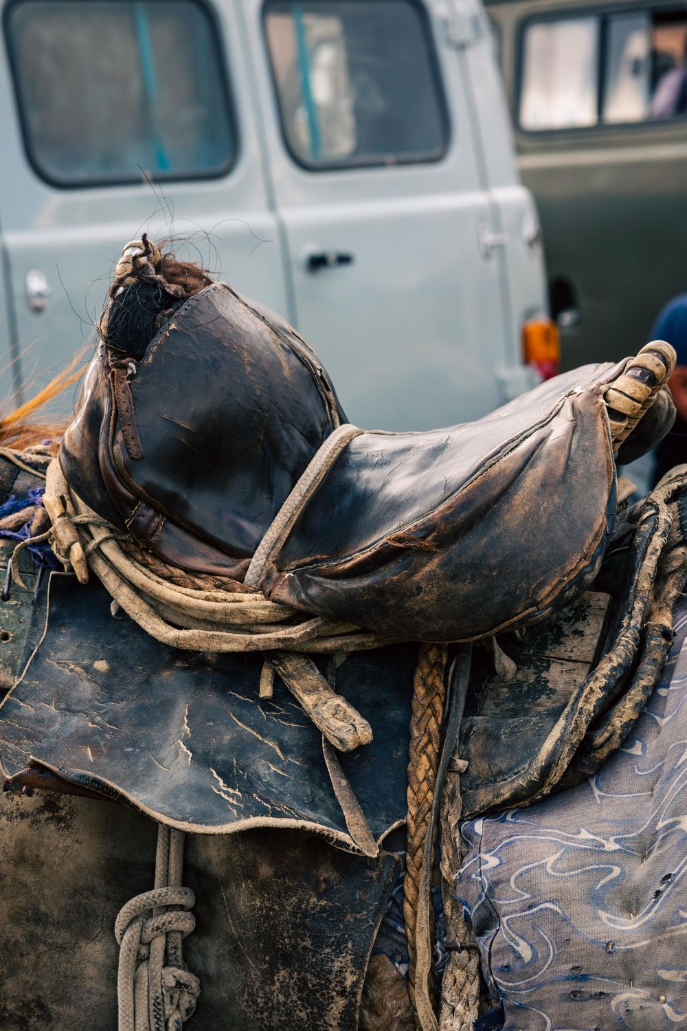 A worn leather horse saddle showing weathered details and patina against a light colored vehicle background.
