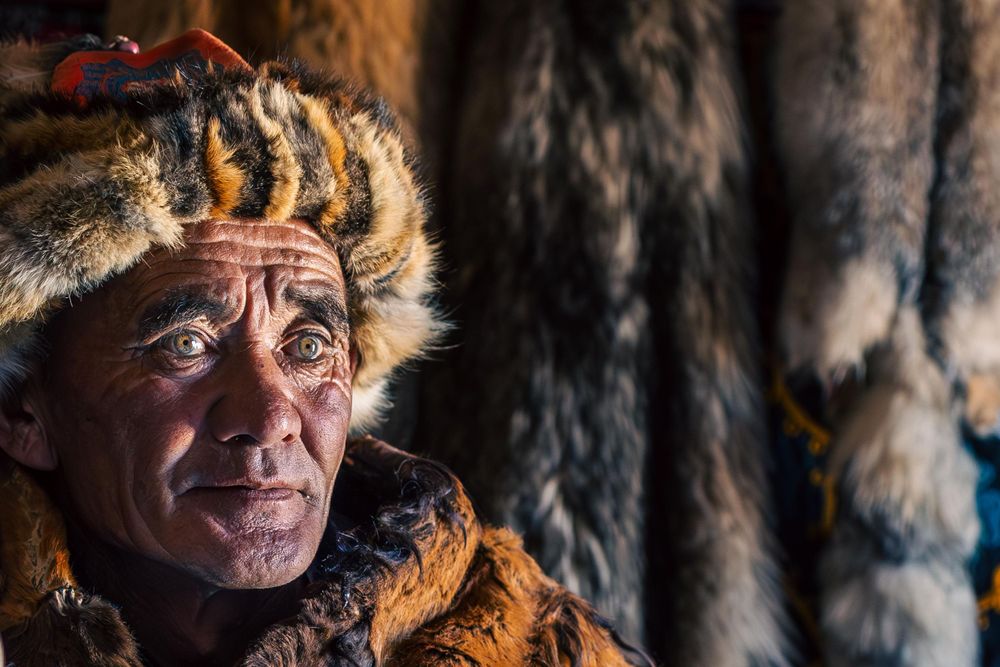 A portrait of someone in traditional fur winter clothing against a dark background.